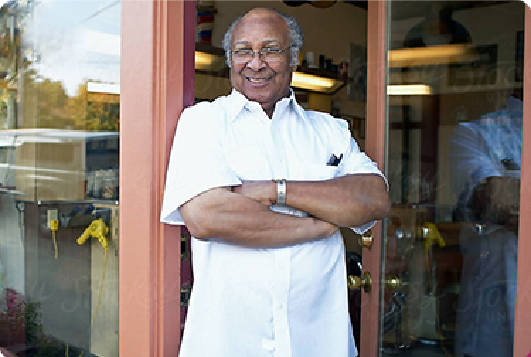 older man with glasses smiling with his arms crossed in a shop doorway