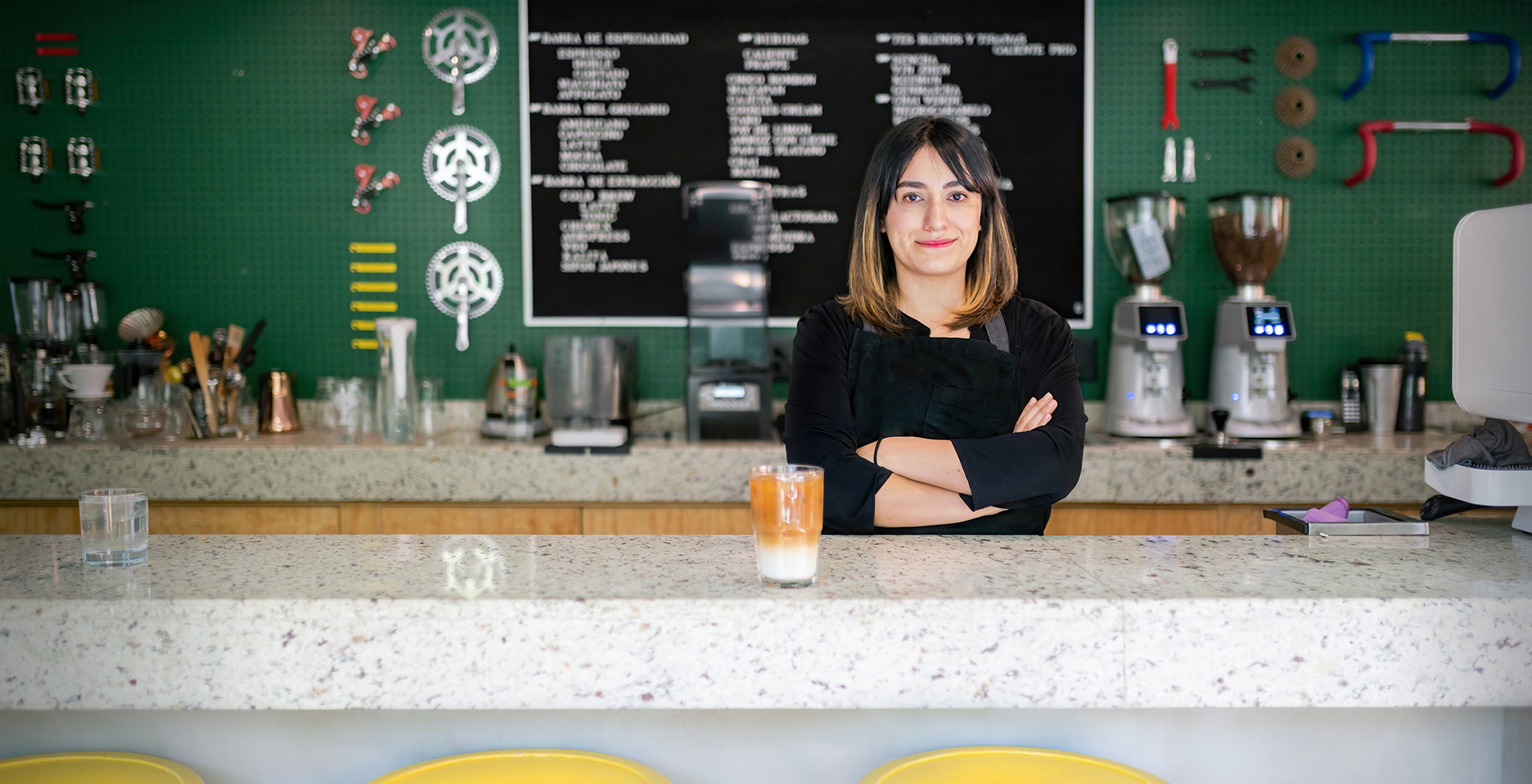 woman standing behind a coffee shop counter with her arms folded and smiling